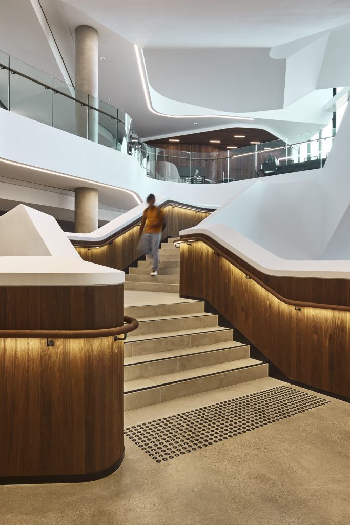 A student walking down a staircase with a balustrade panel made from Satinplank timber lining, with lights glowing beneath the handrail.