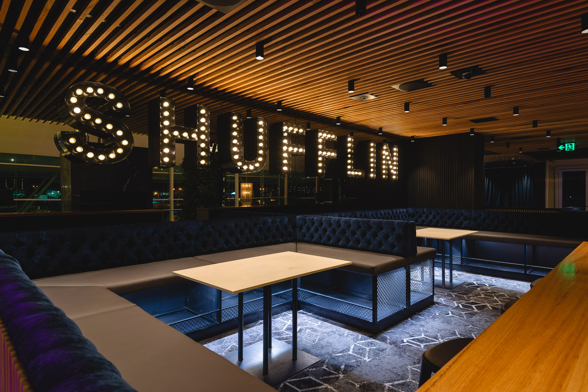 A suspended/dropped ceiling in a bar with a light up sign that reads “Shufflin”.