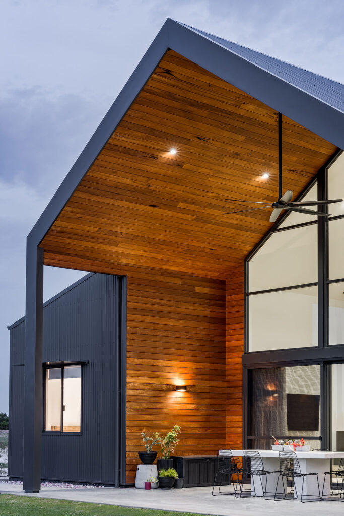 A raked ceiling in an alfresco area with Trendplank cladding contrasting with the dark Colorbond, with recessed downlights and a ceiling fan